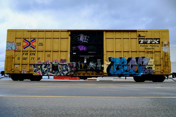 A yellow conex railcar with colorful graffiti.