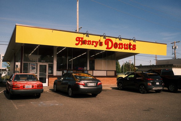 The exterior of a donut shop called "Henry's Donuts" with a yellow awning and several cars parked in front.